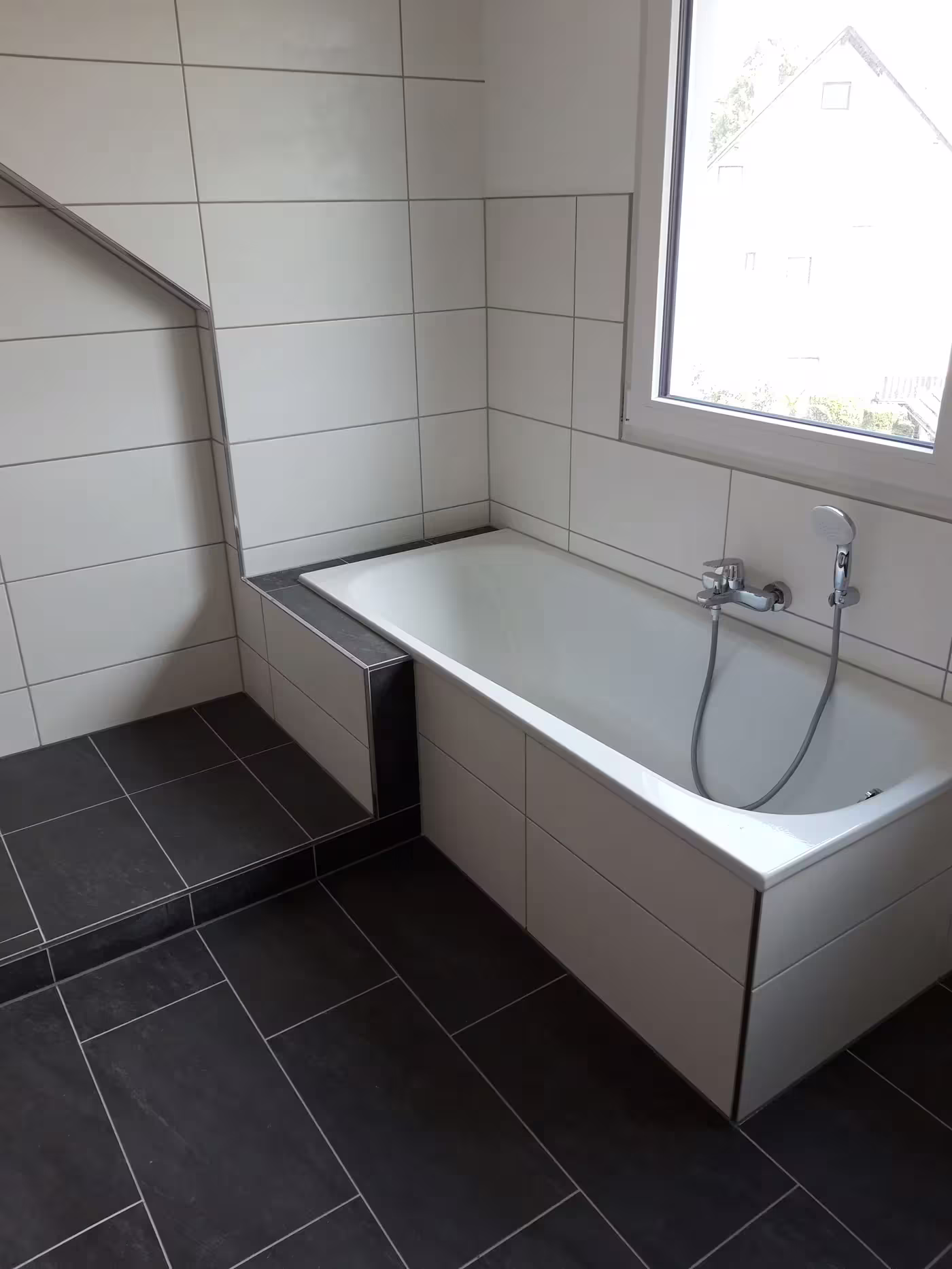 Fertiges Badezimmer mit Badewanne und dunklem Fliesenboden